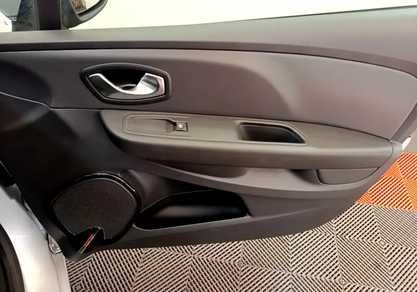 Vue intérieure côté gauche de la porte avant d'une Renault Clio Business gris clair avec haut-parleur intégré et poignée chromée.