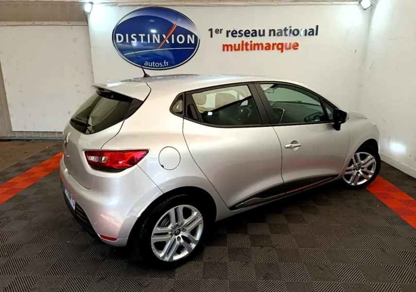 Renault Clio Business TCe 90 gris clair vue 3/4 arrière droit dans un showroom avec logo Distinxion en arrière-plan