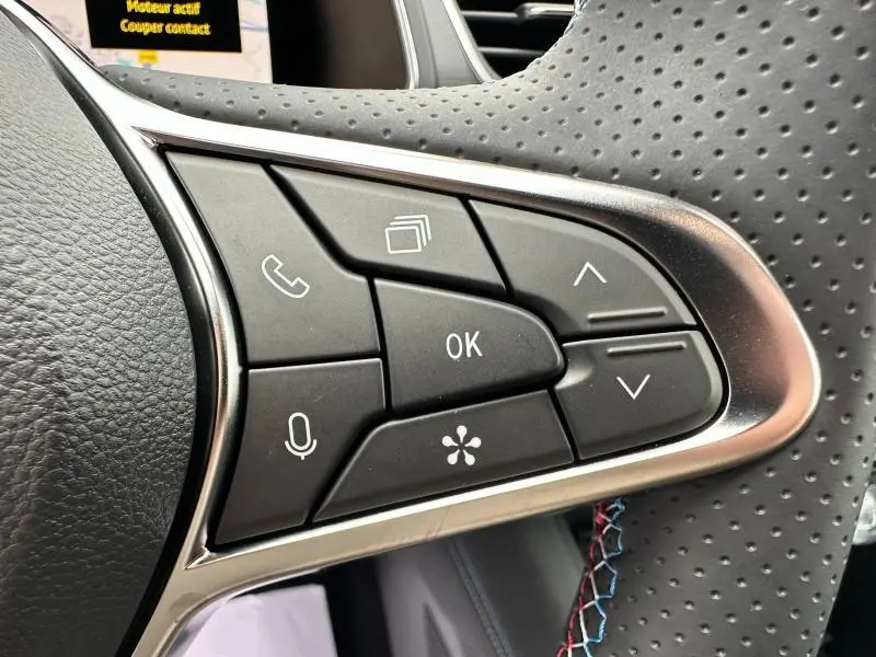 Gros plan sur les commandes du volant côté droit du Renault Captur 2025 esprit Alpine avec cuir perforé et surpiqûres tricolores.