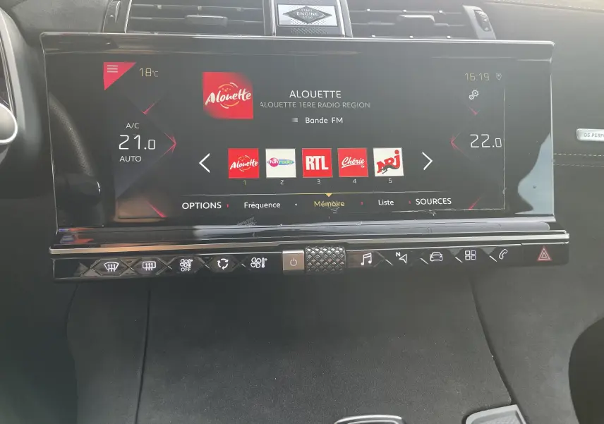 Vue rapprochée de l'écran tactile central et des commandes du tableau de bord du DS7 gris, affichant la radio FM et la climatisation.