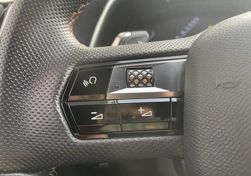 Gros plan sur les commandes du volant perforé noir du DS7 gris, avec boutons de volume et commande vocale.