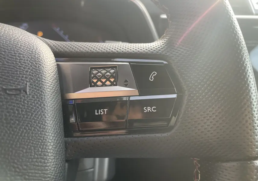 Gros plan sur les commandes gauche du volant perforé noir du DS7 gris, avec boutons LIST et SRC visibles.