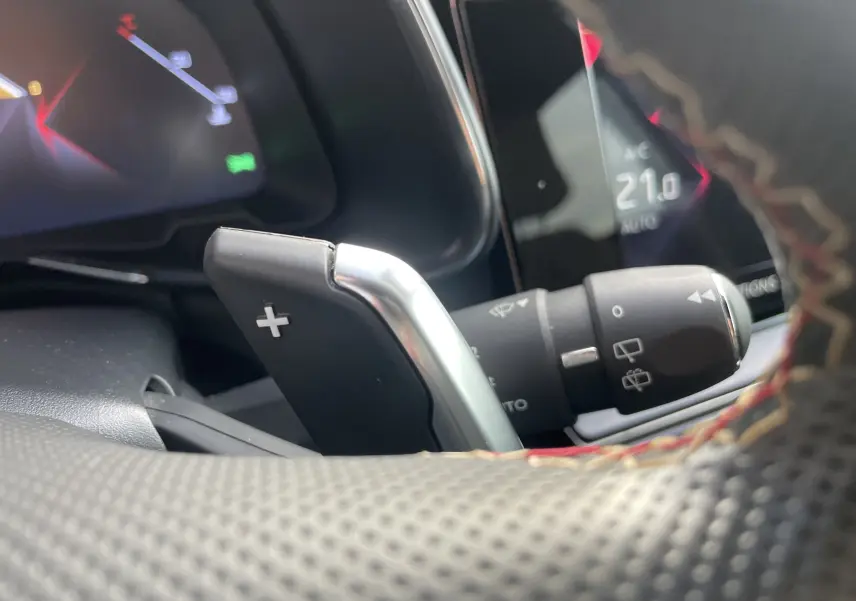 Gros plan sur la palette de changement de vitesse + au volant perforé avec surpiqûres rouges du DS7 gris, tableau de bord en arrière-plan.