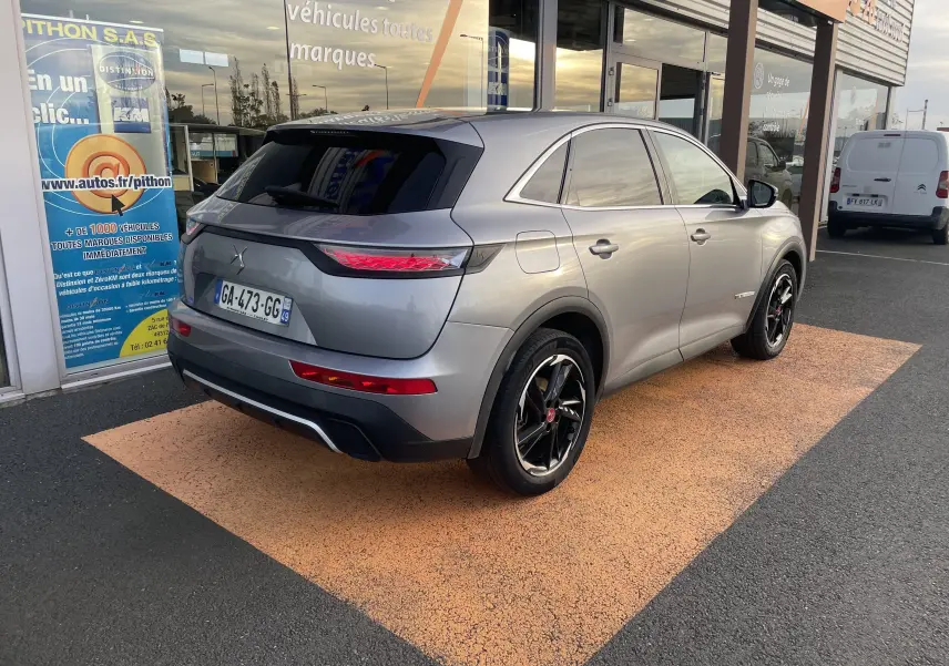 DS7 gris 3/4 arrière droit, avec jantes noires et feux arrière LED, stationné devant un showroom.