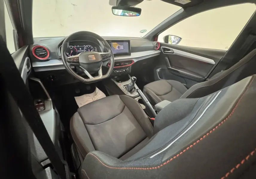 Intérieur de la SEAT IBIZA 1.0 TSI 110 FR vu côté conducteur, sièges noirs avec surpiqûres rouges et volant multifonctions.