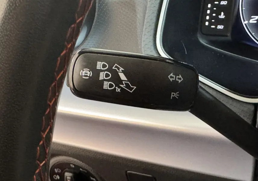 Gros plan sur la manette de clignotants noire avec marquages blancs, volant cuir rouge et tableau de bord partiel d'une SEAT Ibiza 2024.