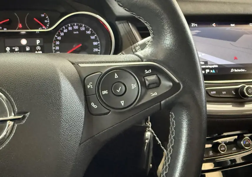 Gros plan sur le volant cuir noir de l’Opel Grandland X 2021 avec commandes multifonctions et écran tactile en arrière-plan.