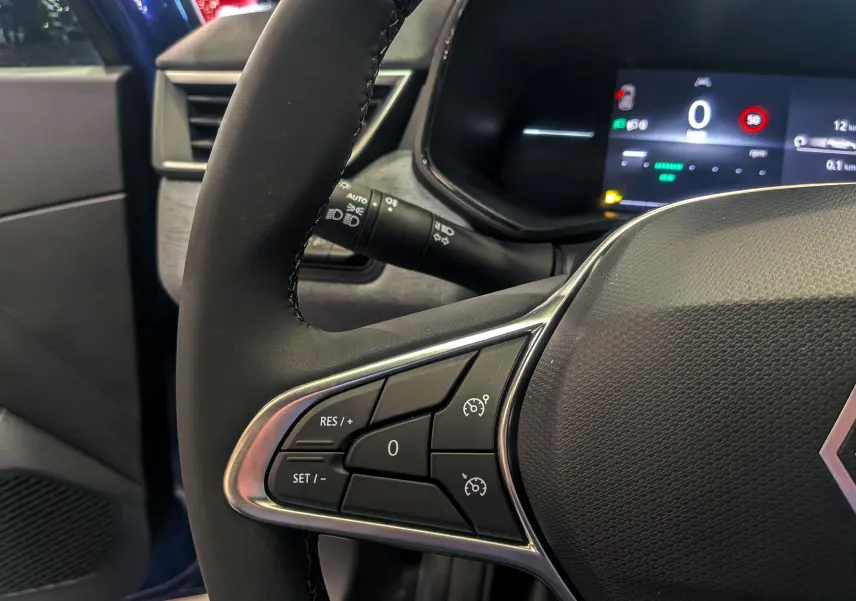 Gros plan sur le volant côté gauche de la Renault Clio V Bleu Iron 2025, avec commandes de régulateur de vitesse et tableau de bord numérique.