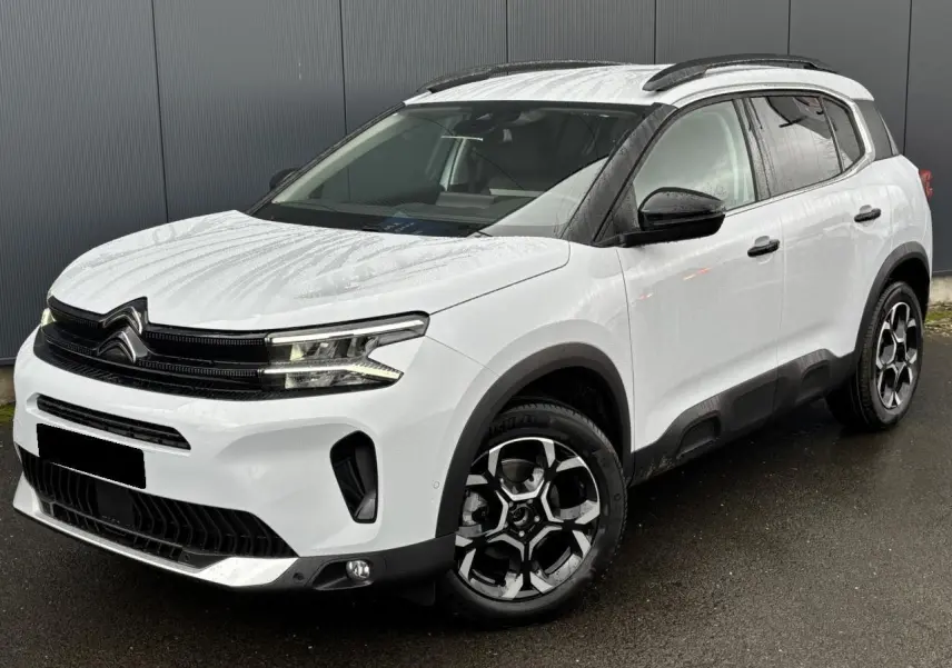 Vue 3/4 avant droit d'un Citroën C5 Aircross blanc Okénite avec jantes alliage bi-ton et barres de toit noires.