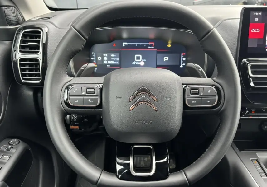 Vue intérieure centrée sur le volant noir cuir du Citroën C5 Aircross 2025 avec tableau de bord numérique et écran tactile.
