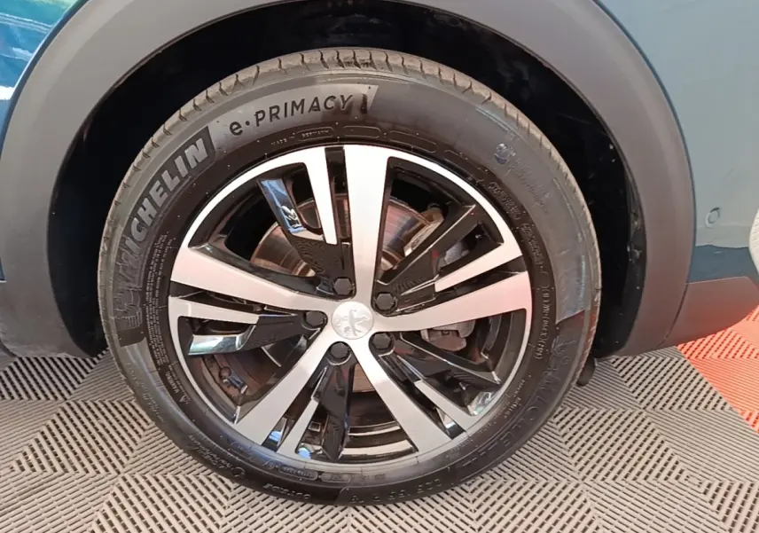 Gros plan sur la roue avant droite du Peugeot 3008 bleu, jante alliage bicolore et pneu Michelin e-Primacy.