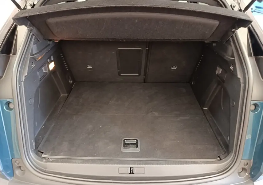 Coffre ouvert vu de l'arrière d'un Peugeot 3008 bleu hybride rechargeable, avec plancher plat et intérieur noir.