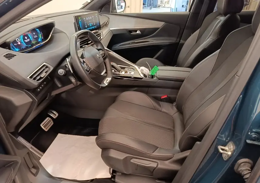 Vue intérieure côté conducteur du Peugeot 3008 hybride bleu 2022, avec tableau de bord digital et sièges en tissu noir.