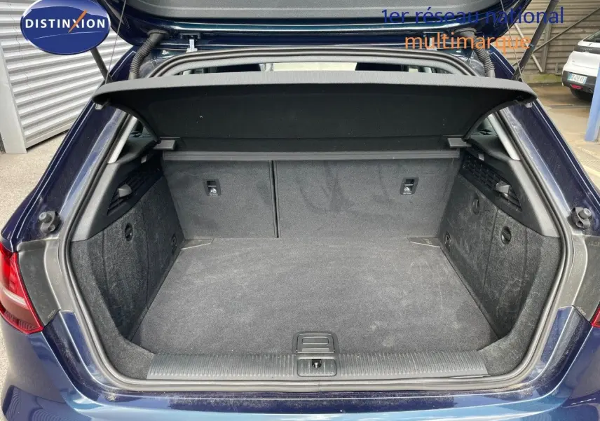 Coffre ouvert d'une Audi A3 Sportback bleu cosmos métal, vue arrière montrant l'espace de chargement vide et la plage arrière.