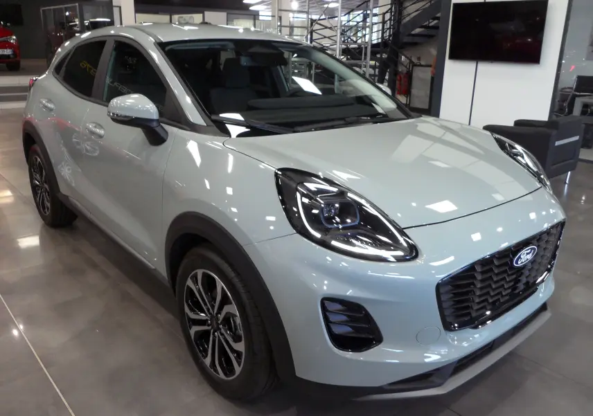 Ford Puma 2025 gris Cactus en 3/4 avant droit, avec phares LED et calandre noire brillante dans un showroom.