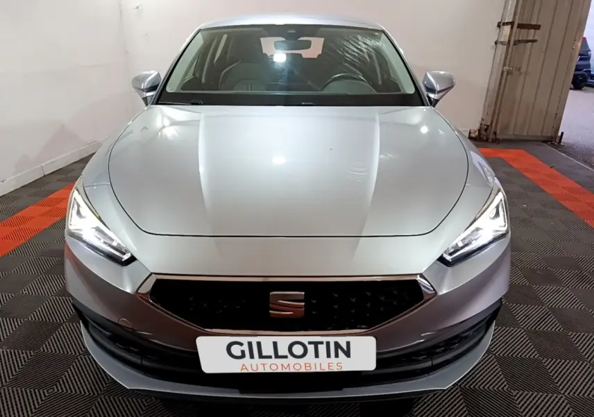 Vue frontale d'une SEAT Leon gris clair avec phares LED allumés et calandre noire hexagonale.