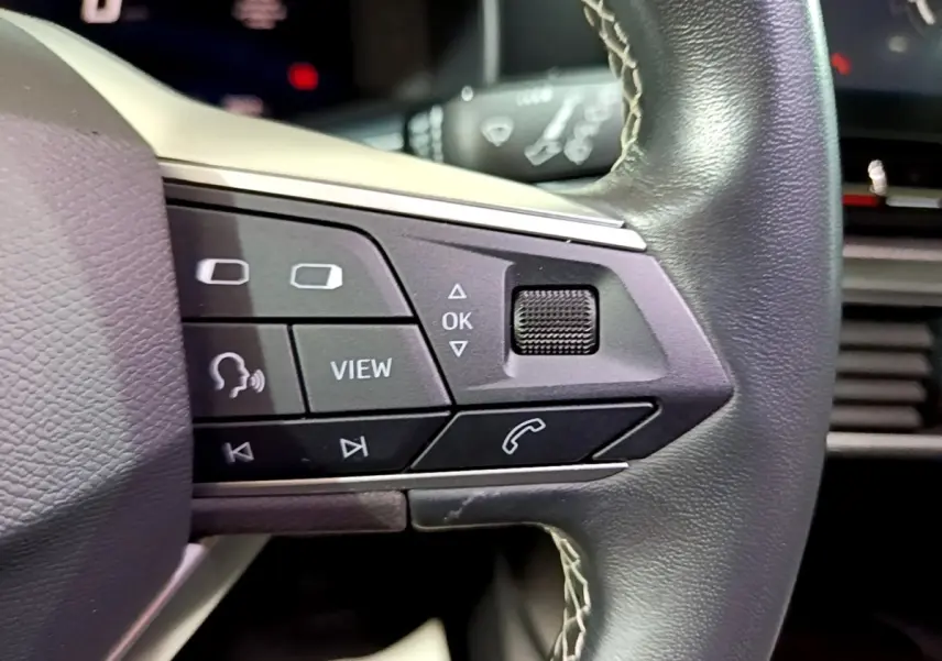 Gros plan sur les commandes gauche du volant cuir du SEAT LEON gris clair 2023 avec boutons multifonctions visibles.