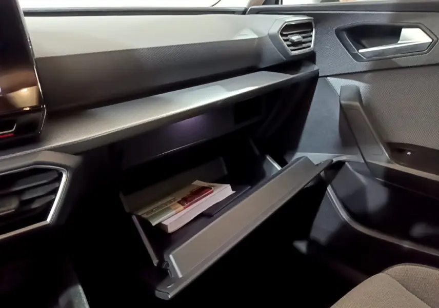 Vue intérieure côté passager du SEAT Leon 2023, boîte à gants ouverte avec documents, ambiance sombre et moderne.