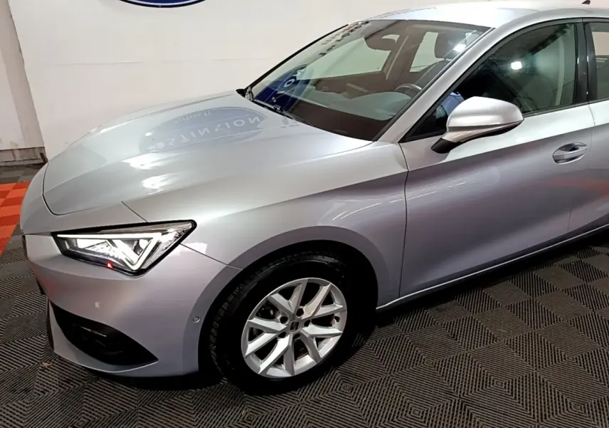 Vue 3/4 avant droit d'une SEAT Leon gris clair avec phares LED et jantes alliage en showroom.