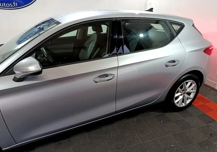 Profil côté gauche d'une SEAT LEON gris clair 2023, avec jantes alliage et vitres teintées dans un showroom.