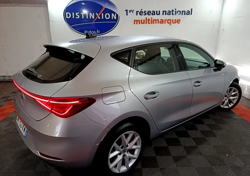 Vue 3/4 arrière droite d'une SEAT Leon gris clair 2023 avec feux LED et jantes alliage dans un showroom.