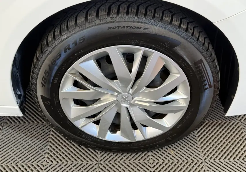 Gros plan sur la roue avant droite d'une Peugeot 208 blanche, avec jante argentée et pneu Pirelli visible.