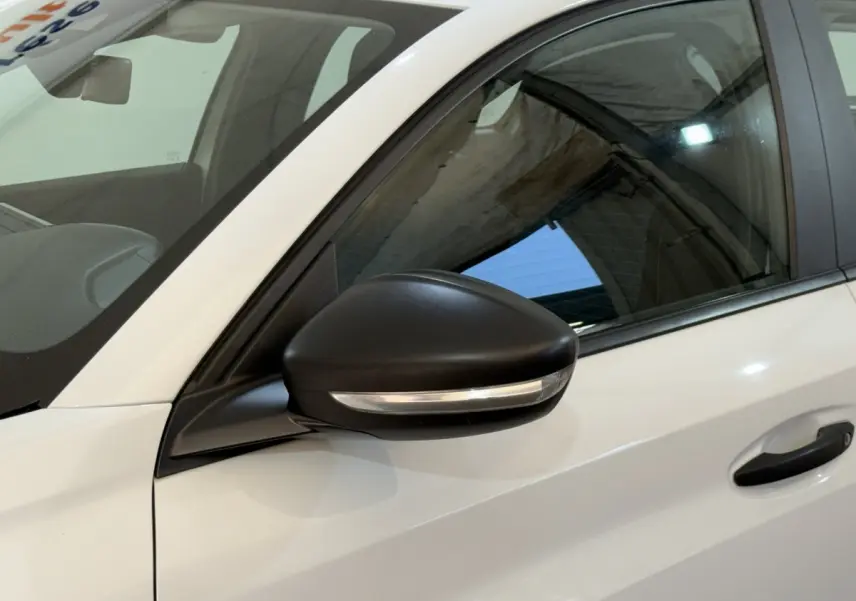 Vue rapprochée du côté gauche avant d'une Peugeot 208 PureTech 75 S&S Like blanche avec rétroviseur noir et clignotant intégré.