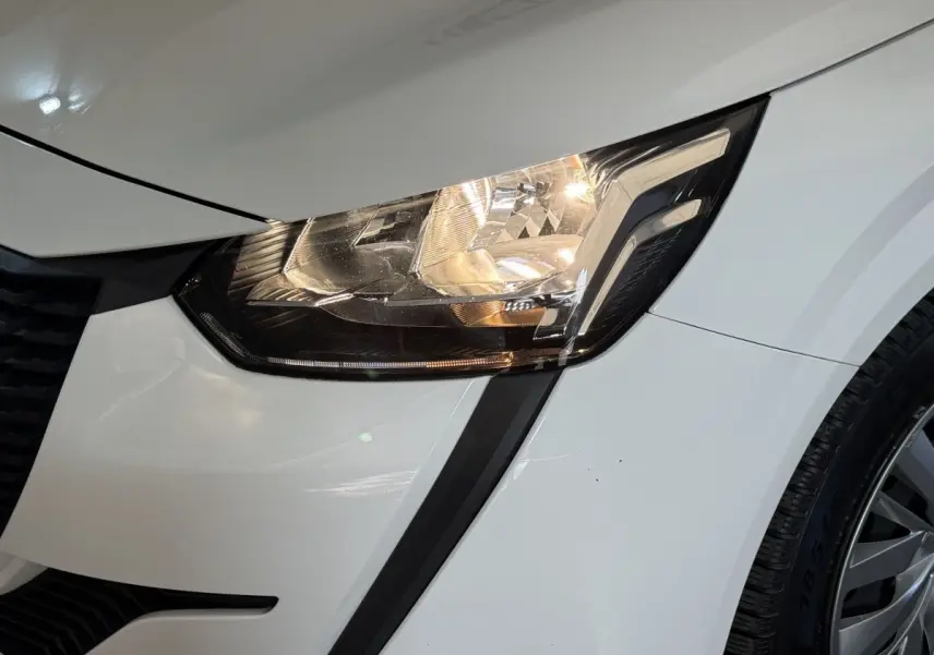 Gros plan sur le phare avant droit allumé d’une Peugeot 208 PureTech 75 S&S Like blanche de 2020.