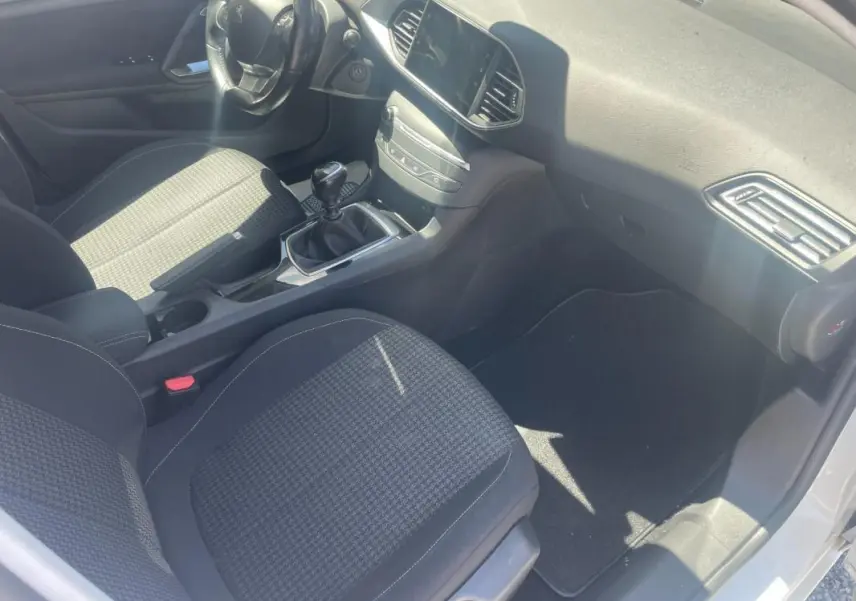 Intérieur avant droit de la Peugeot 308 blanche, montrant sièges tissu, tableau de bord et levier de vitesse manuel.
