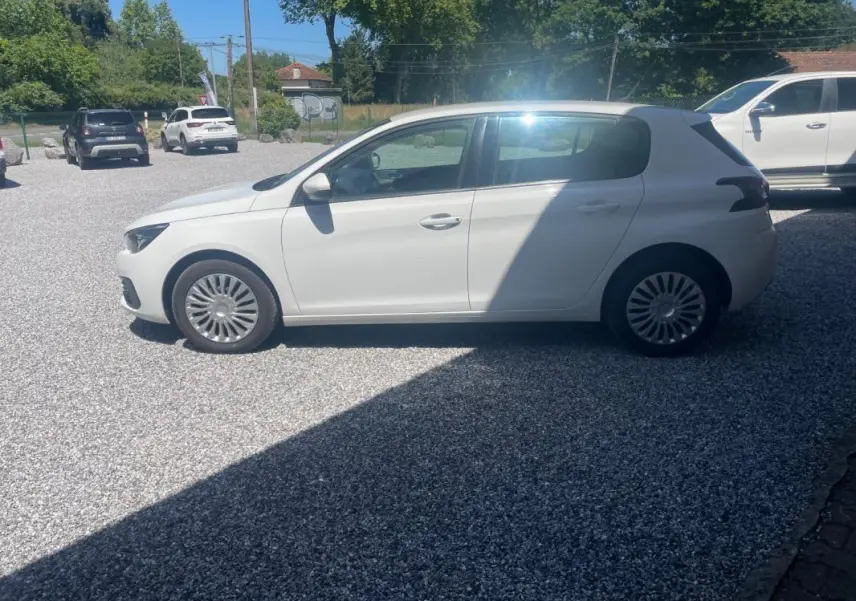 Peugeot 308 blanc vue de profil côté gauche sur un parking extérieur, avec jantes à rayons fins.