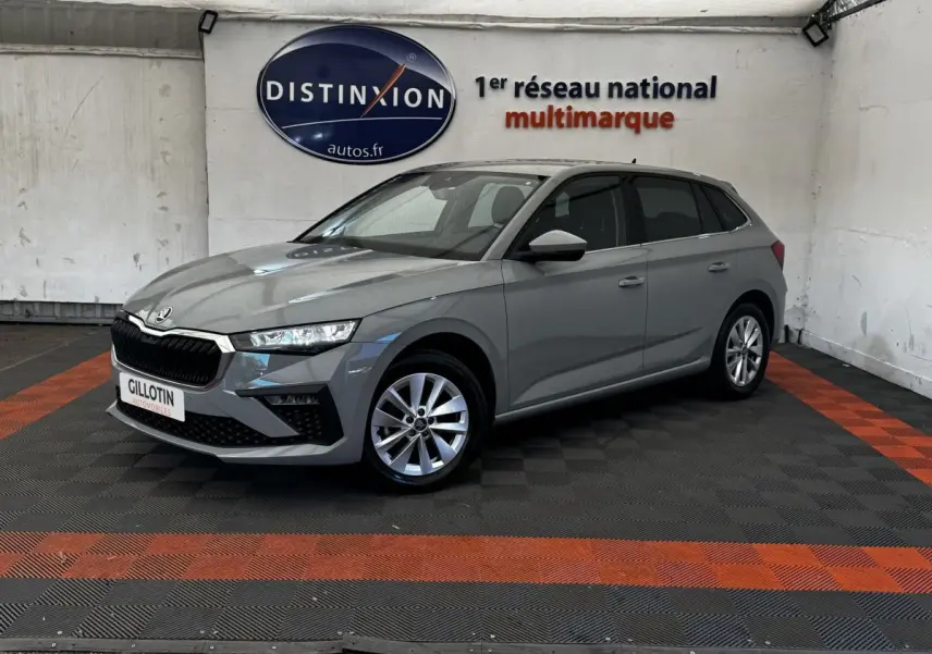 Vue 3/4 avant droite d'une Skoda Scala gris clair stationnée en intérieur avec jantes alliage et calandre noire distinctive.