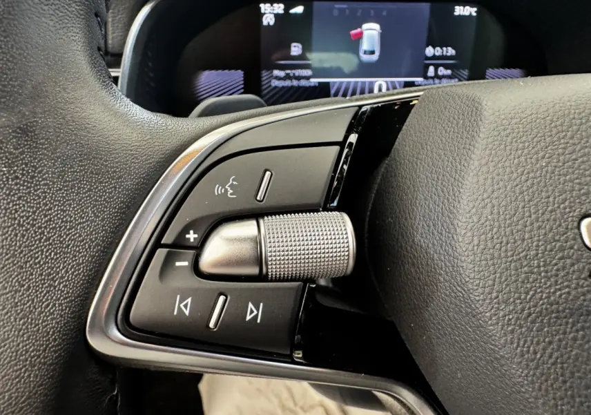 Gros plan sur la molette de commande et boutons multifonctions côté gauche du volant en cuir noir d'une Skoda Scala gris clair.