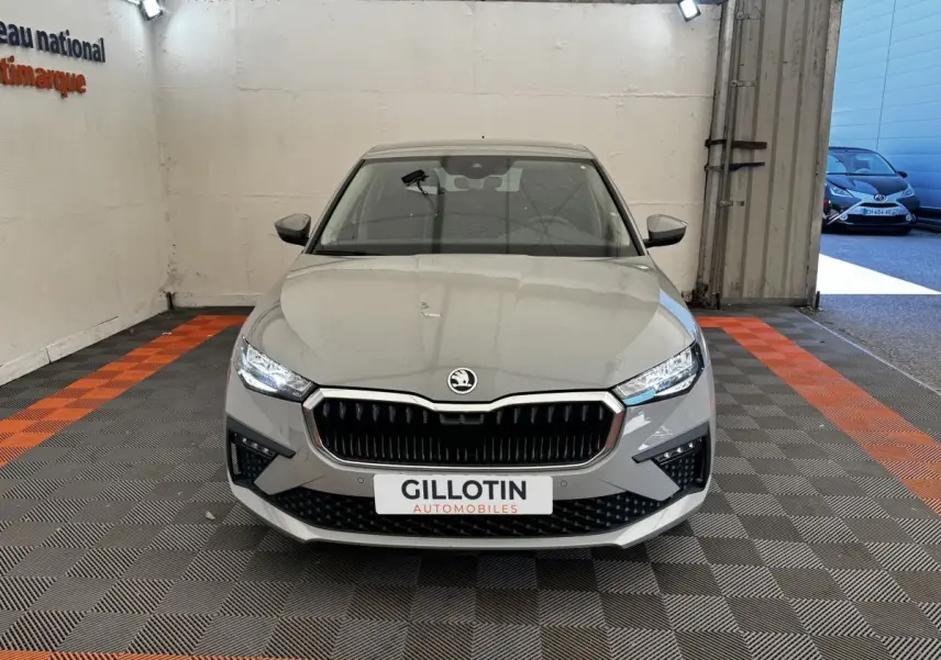 Vue frontale d'une Skoda Scala gris clair avec calandre noire et phares LED allumés en intérieur showroom.