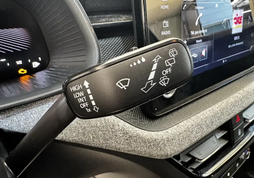Gros plan sur la commande des essuie-glaces dans l’habitacle gris clair du Skoda Scala 2025, avec écran tactile en arrière-plan.