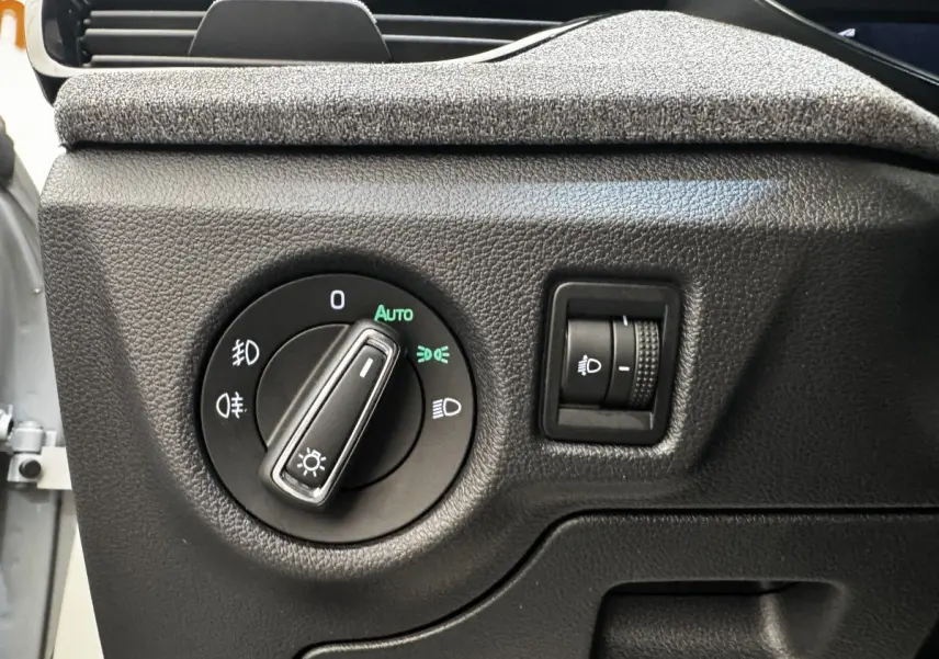 Gros plan sur la commande des phares avec réglage d'intensité dans une Skoda Scala gris clair, intérieur noir texturé.