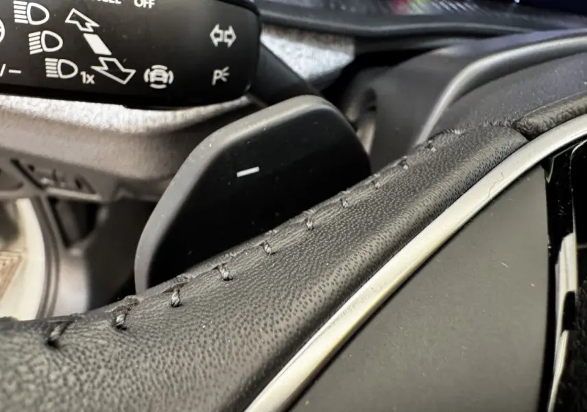 Gros plan sur la palette de changement de vitesse derrière le volant cuir du Skoda Scala gris clair, détails des commandes visibles.