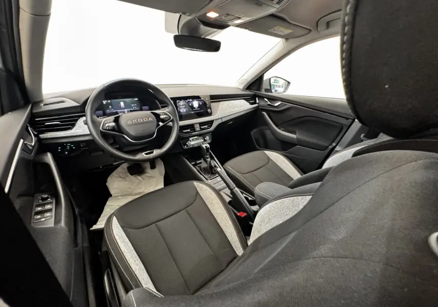 Vue intérieure avant droite de la Skoda Scala 2025, sièges bicolores gris clair et noir, tableau de bord moderne avec écran tactile.