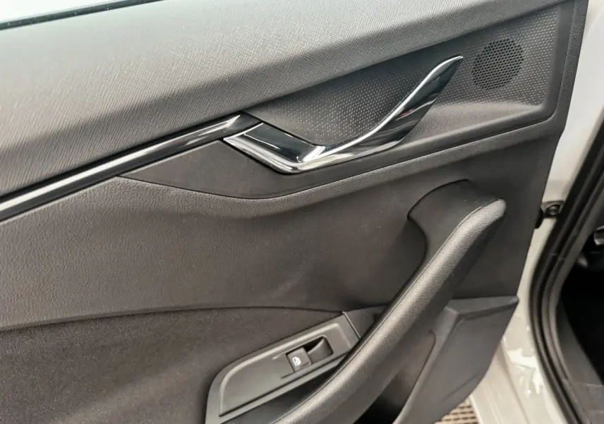 Intérieur côté gauche de la porte avant d’une Skoda Scala gris clair, avec poignée chromée et commande de fenêtre.