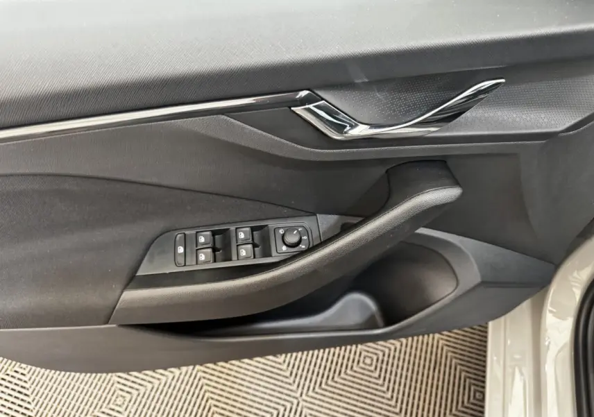 Vue rapprochée de la porte avant gauche de la Skoda Scala gris clair, avec commandes des vitres et poignée noire.