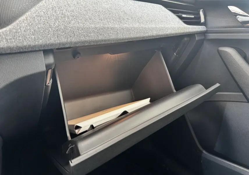 Gros plan sur la boîte à gants ouverte côté passager du Skoda Scala gris clair, montrant l'intérieur et un manuel.