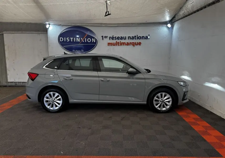 Vue de profil côté gauche d'une Skoda Scala gris clair 2025 stationnée en intérieur avec jantes alliage et feux arrière distinctifs.