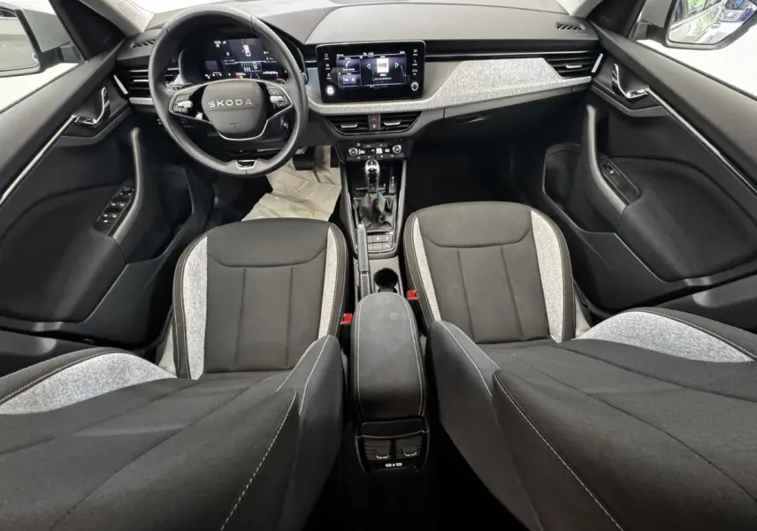 Vue intérieure avant de la Skoda Scala 2025, tableau de bord moderne avec écran tactile et sièges bicolores gris et noir.
