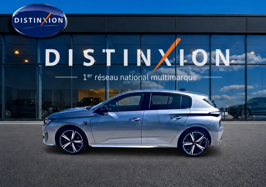 Peugeot 308 gris en profil droit, avec jantes alliage et toit légèrement incliné, devant une vitrine Distinxion.