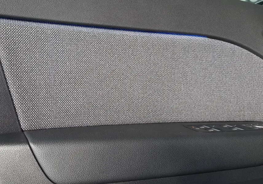 Détail de la garniture intérieure côté gauche de porte du Renault Captur E-Tech Hybrid 2024 avec tissu gris et éclairage bleu.