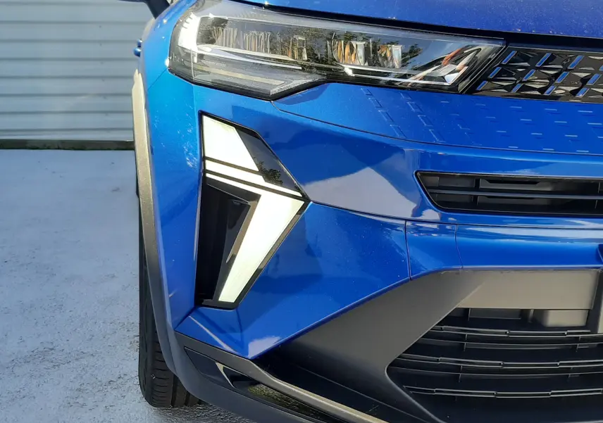 Gros plan sur l'avant gauche du Renault Captur E-Tech Hybrid 2024 bleu iron avec feux LED en forme de flèche.
