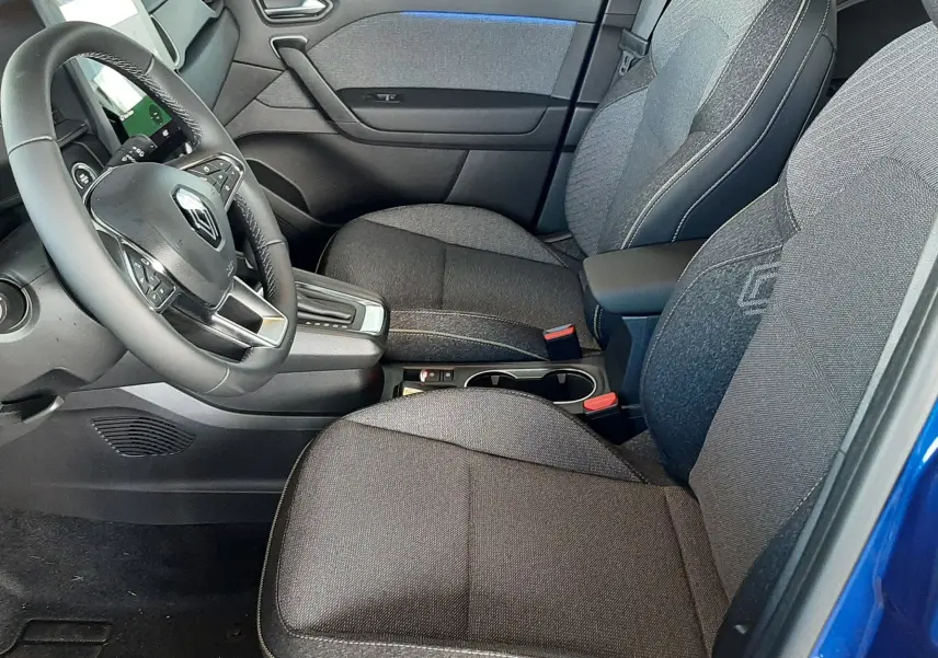 Intérieur avant droit du Renault Captur E-Tech Hybrid 2024, sièges gris foncé avec surpiqûres et détails bleus, volant multifonction.