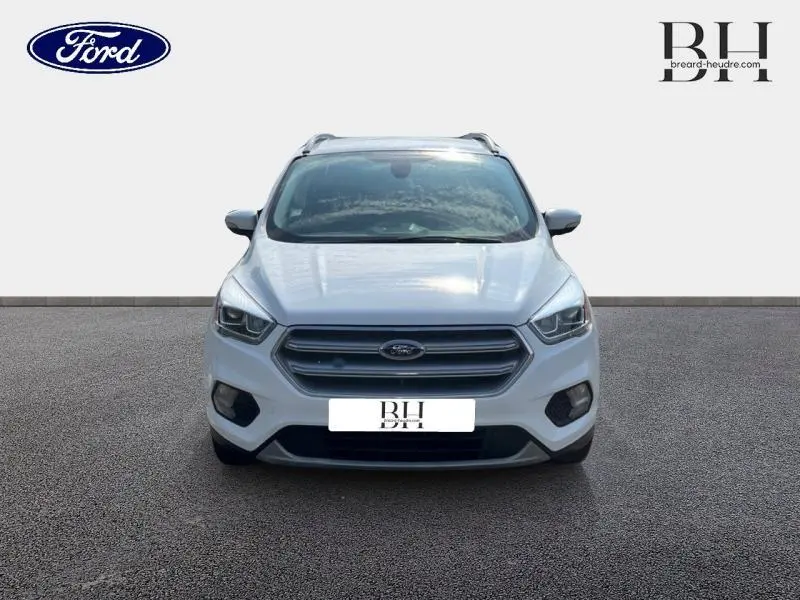 Vue frontale d'un Ford Kuga blanc glacier avec calandre grise et barres de toit visibles sur fond neutre.