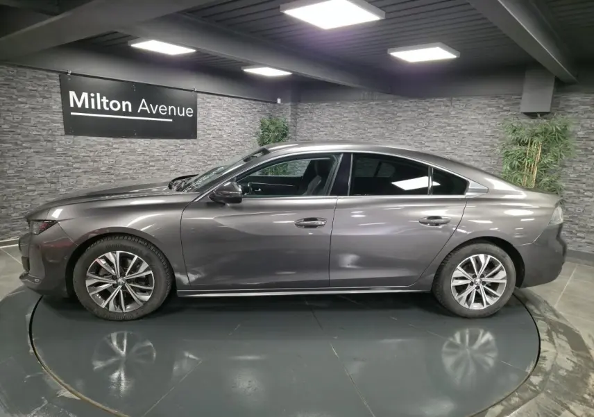 Profil côté gauche d'une Peugeot 508 gris métallisé 2018 avec jantes alliage et vitres surteintées en intérieur showroom.