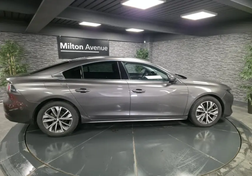 Profil côté gauche d'une Peugeot 508 gris métallisé, avec jantes alliage et lignes élégantes dans un showroom.