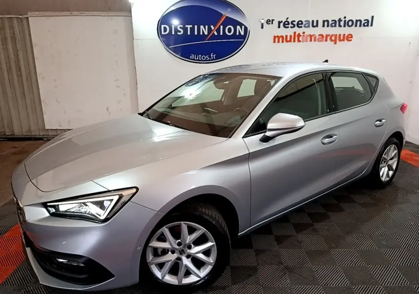 SEAT Leon gris foncé vue 3/4 avant droit dans un showroom avec éclairage intérieur et logo Distinxion en arrière-plan